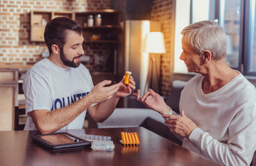 Professional consultation. Confident skilled pleasant volunteer sitting by the table opposite another man holding and demonstrating pills.