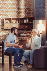 Friendly conversation. Sociable attentive beardful man sitting in the bright room on the chair smiling and talking to a retired.