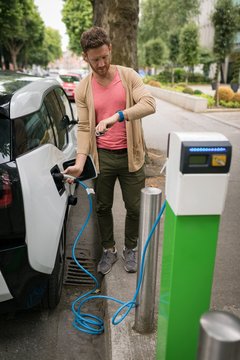 Man checking time on smart watch while charging electric car