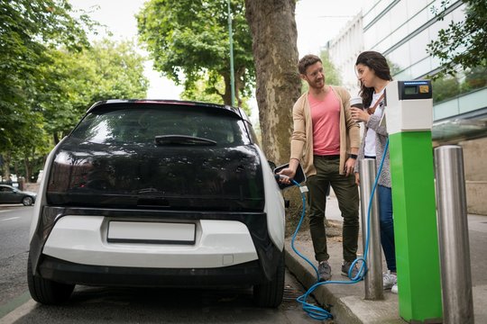 Couple interacting with each other while charging electric car 