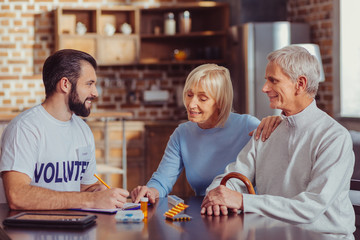 Fototapeta premium Explain please. Curious interested gray haired woman sitting by the table listening to a volunteer and pointing at notebook.