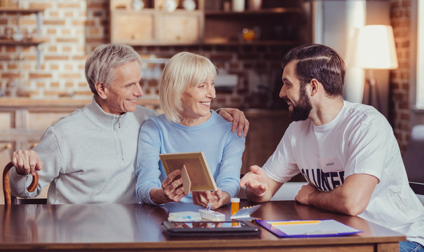 Tell a story. Interested unshaken friendly man sitting by the table smiling and listening to a married couple.