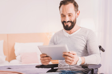 Rise your mood. Positive handsome disabled man holdigng a tablet while surfing the net at home