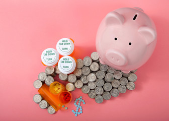 flat lay of Pink piggy bank next to stacks of coin cash piled high around Rx prescription drugs, pills spilled onto pink surface in shape of dollar sign, pink background. Cost of health care concept.