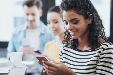 Online life. Joyful three friends using smartphones while gazing down