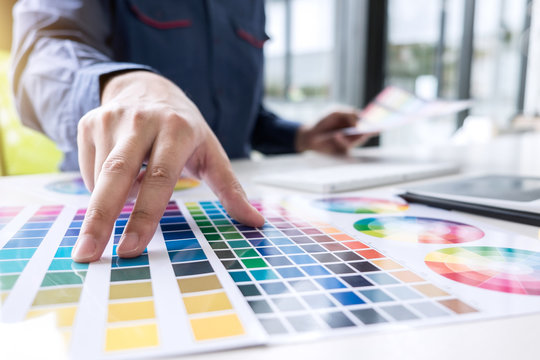 Male creative graphic designer working on color selection and color swatches, drawing on graphics tablet at workplace with work tools and accessories