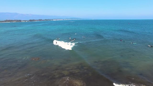 Low drone shot of a surfer riding a wave in Goleta, California. Many other surfers waiting to catch a wave for themselves