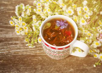 Herbal tea in a cup and bouquet of field camomiles on an old wooden surface, toned. Phytotea from autumn herbs. Traditional medicine. 