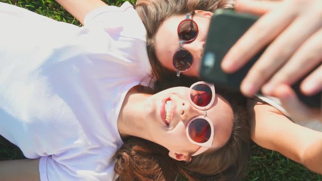 Top view of young woman friends having video chat lying on back sharing travel adventure smiling laughing at beach direct from above - summer fashion, leisure and technology concept