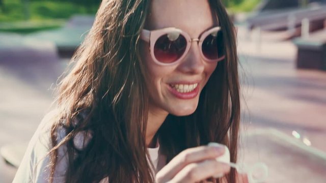 Portrait of young woman in sunglasses blowing bubbles and having fun on outdoors. Cinematic slow motion, young festival woman blowing bubbles, summer lifestyle