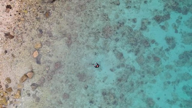 Drone shot of a seemingly beautiful tropical beach, but one can notice the dead corals that appears as tiny black stones on the seabed.