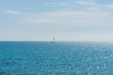 Seascape with blue water in Spain on a summer day. Sailboat on the horizon at the Mediterranean Sea