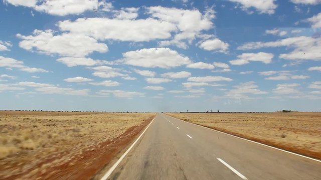 Camper van with dirty glass driving through splendid desert landscape of empty road and blue sky with clouds in Outback Australia of Queensland rural area. Road trip adventure, no traffic concepts