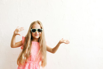 Little girl w/ long golden hair in fashionable casual outfit, wearing sunglasses & smiling, laughing, making funny faces. Five years old daughter in pink dress posing. Background, close up, copy space