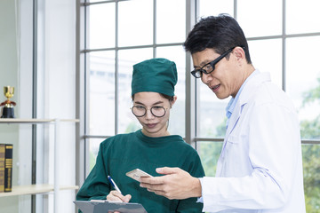 Young woman medical student writing documents about research.Professor holding phone in whit suit and glasses at laboratory.Student in green suit.Copy space.