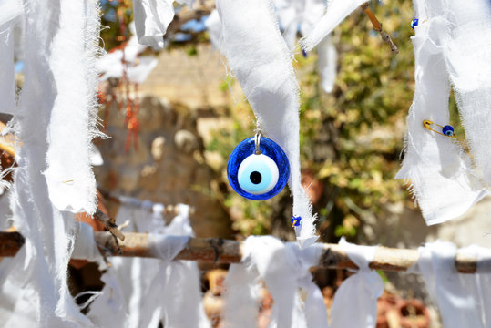 Blue evil eye amulet hanging among white fabric strips outdoors, symbolizing protection, tradition, and cultural belief with a soft natural background.