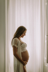 Young pregnant woman standing by the window