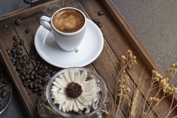Espresso cup,coffee bean and dried flowers jar on wooden tray with warm morning light near the window.Copy space.