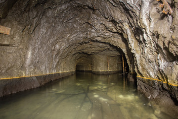 Naklejka premium Underground abandoned gold iron ore mine shaft tunnel gallery passage with timbering wooden flooded water
