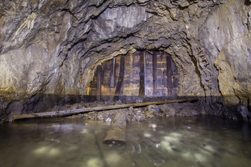 Naklejka premium Underground abandoned gold iron ore mine shaft tunnel gallery passage with timbering wooden flooded water
