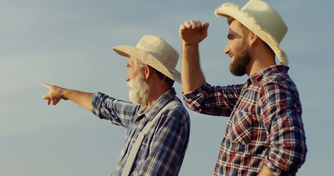 Caucasian farmers, son and father, standing in the field at the end of the summer, old man pointing at something and telling something.