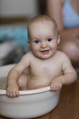 baby boy indoor bathing in the small white bathtub . He is smiling and full of happiness