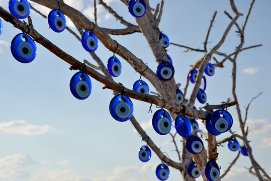 Evil eye beads hanging on a dry tree branch under a blue sky, traditional Turkish Nazar amulets for protection and good luck, spiritual culture of Turkey