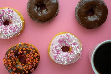 Colorful donuts on a pink table being served for breakfast with piping hot coffee.