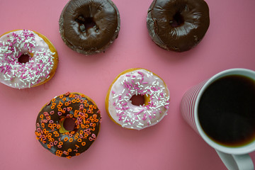 Colorful donuts on a pink table being served for breakfast with piping hot coffee.