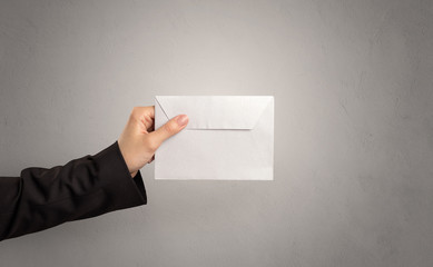 Female hand holding coloured and white envelope with empty wall background
