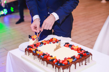the groom takes a piece of wedding cake on a plate. Rectangular wedding cake