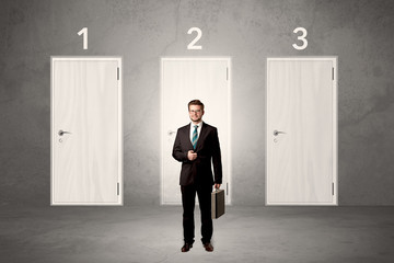 Fototapeta premium Businessman in grey room with three numbered white door behind his back 