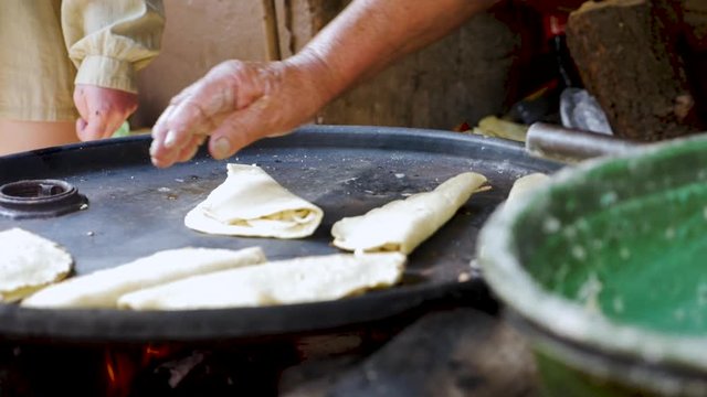 Woman flipping quesadillas by hand on a oil barrel lid as a comal