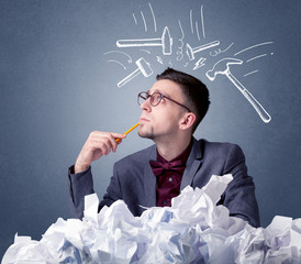 Young businessman sitting behind crumpled paper with drawn hammers hitting his head 