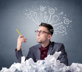Young businessman sitting behind crumpled paper with drawings of gears and steam over his head