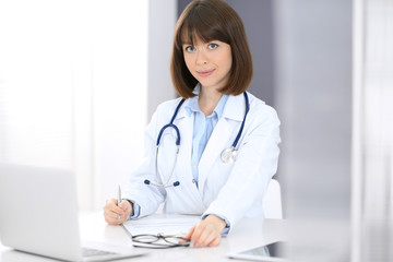 Doctor woman at work. Female physician filling up medical form while sitting the table in clinic or hospital. Medicine and healthcare concept for advertising