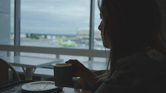 Young woman drinks coffee in airport caffee waiting for departure