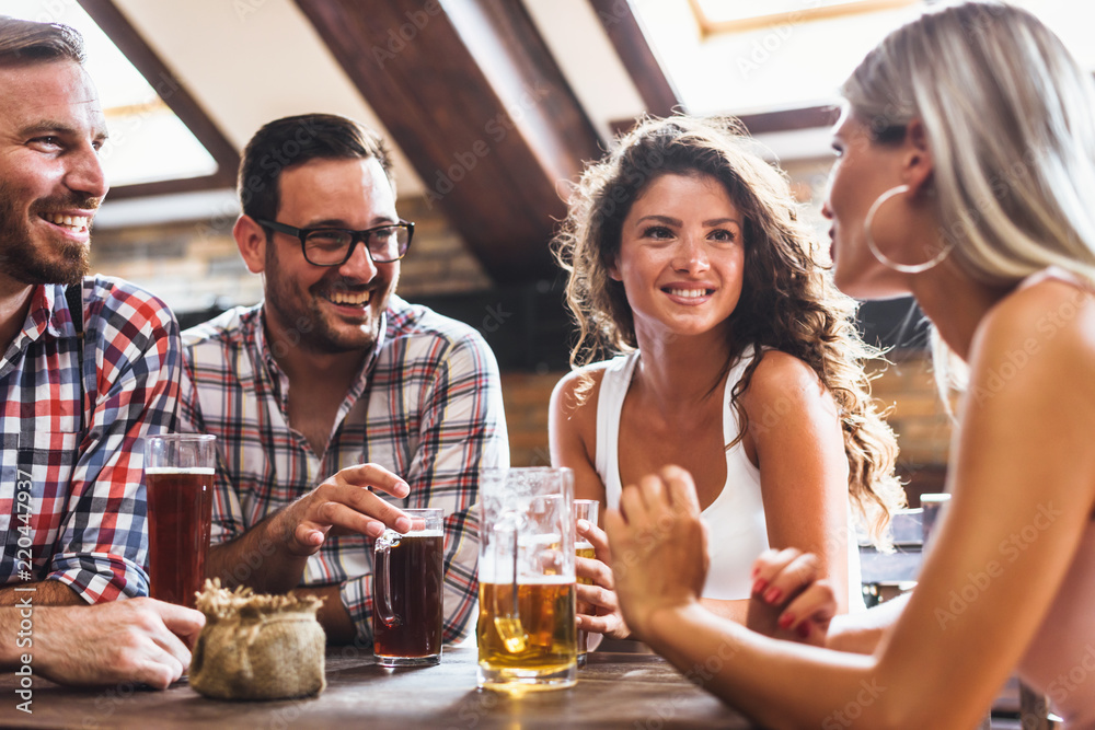 Wall mural Happy friends having fun at bar - Young trendy people drinking beer and laughing together