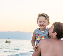 Happy family. Young beautiful father and his smiling son baby boy having fun on the beach of the sea, ocean. Positive human emotions, feelings, joy, kissing.