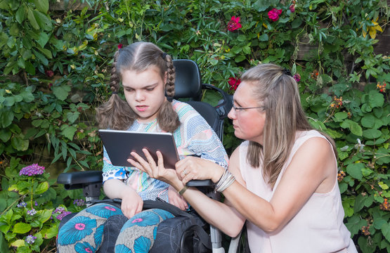 A Disabled Child In A Wheelchair Being Cared For By A Voluntary Care Worker.