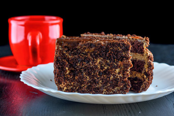 a piece of chocolate cake and cookies with chocolate on a red plate on a dark wooden background. Homemade baking.Close-up view.