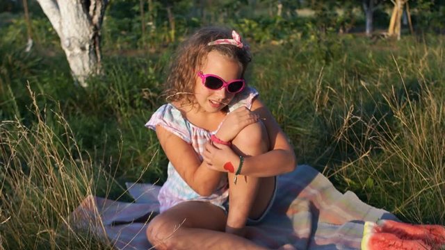 A schoolgirl is sunbathing sitting on the grass. The girl wears sunglasses and a bandage on her head. Picnic in nature. Summer vacation