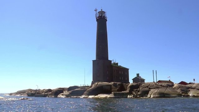 Pov view from a boat of a tall lighthouse, on a rocky island bengtskar, on a sunny summer day, in saaristomeri national park of the finnish archipelago, in Varsinais-suomi, Finland