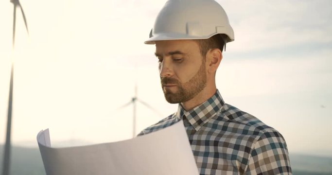 Close up of the handsome wind renewable power station worker in the halmet checking some document and drawing.
