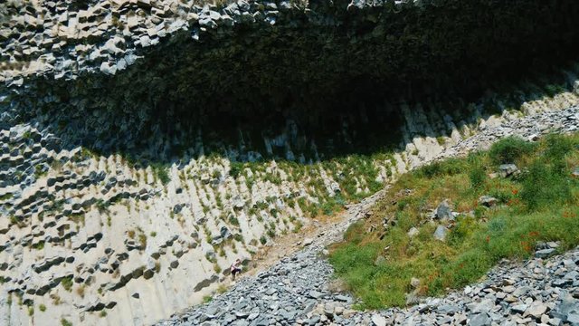 Tourist girl climbes up towards huge overhang of basalt octagonal rocks in Garni Gorge