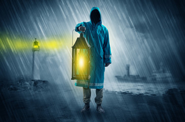 Man at the coast coming in raincoat with glowing lantern concept

