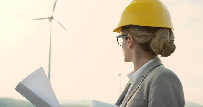 Close up of the beautiful wind renewable power station female worker in the halmet checking some document and drawings.