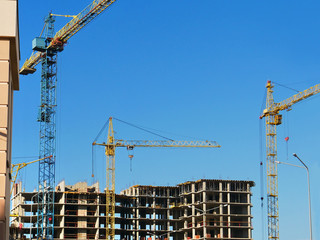 Three tower cranes near concrete building. Construction site.