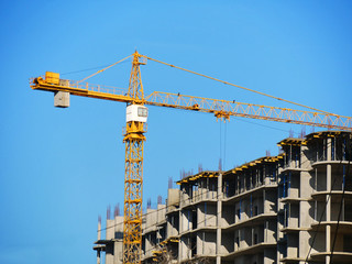 Crane and building against blue sky. Construction site with crane and concrete building.