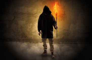 Ugly wayfarer with burning torch in his hand in front of a crumbly wall concept
